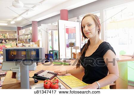 Stock Photo - Woman working in organic food market, serving at cash register. Fotosearch