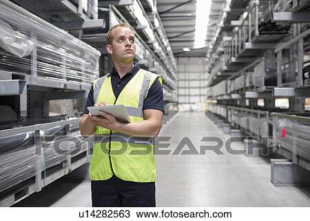 Stock Image - Worker checking order in engineering warehouse. Fotosearch