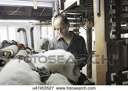 Stock Photo - Worker looking at fleece in wool factory. Fotosearch