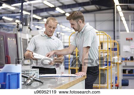 Stock Photo - Workers discussing component in engineering factory. Fotosearch