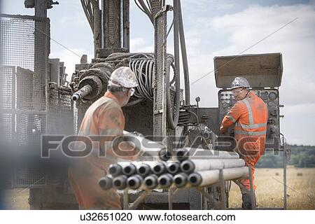 Stock Image - Workers in hard hats operating drilling rig. Fotosearch