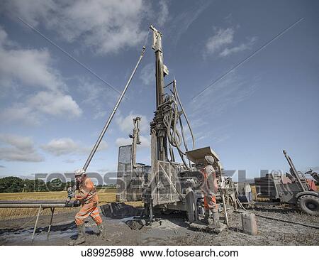 Stock Photo - Workers operating drilling rig to explore for coal in field. Fotosearch