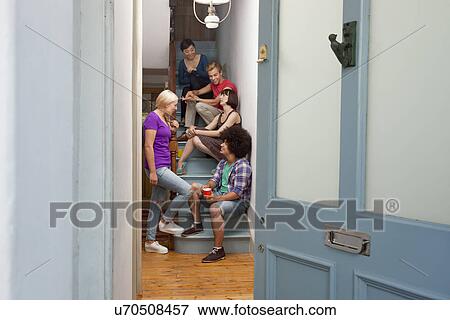 Stock Photo - Young adult flatmates chatting on stairs. Fotosearch