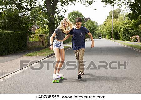 Stock Photograph - Young couple skateboarding on road. Fotosearch