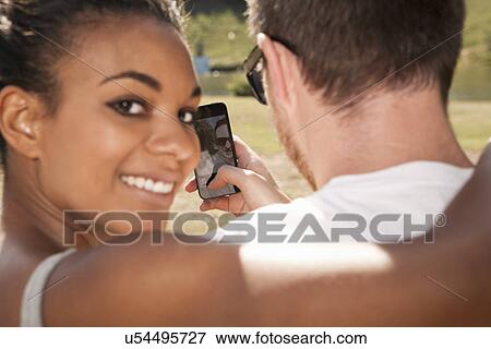 Young couple taking picture of themselves with phone, woman looking over shoulder View Large Photo Image Stock Photo - Young couple taking picture of themselves with phone, woman looking over shoulder. Fotosearch