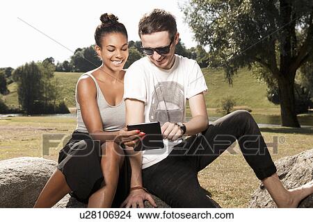 Picture - Young couple using digital tablet in park. Fotosearch