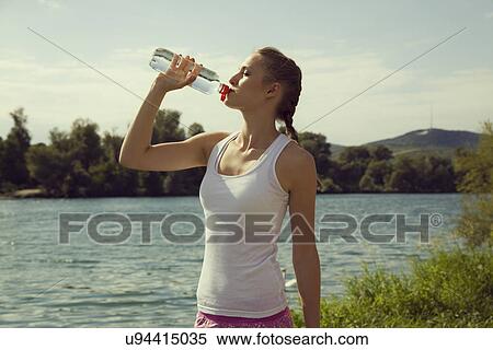 Stock Photography - Young female jogger drinking bottled water. Fotosearch