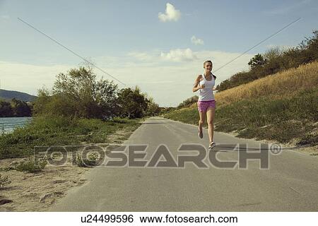 Stock Photograph - Young female jogger running along riverside. Fotosearch