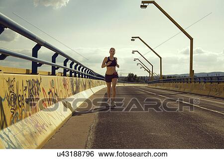Stock Photograph - Young female jogger running on bridge. Fotosearch