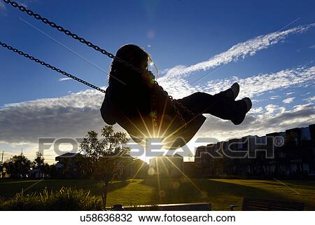 Stock Image - Young girl on swing at sunset. Fotosearch