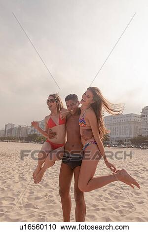 Stock Image - Young man carrying two women together on Copacabana Beach, Rio de Janeiro, Brazil. Fotosearch