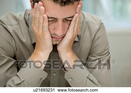 Stock Image - Young man covering cheeks with hands. Fotosearch