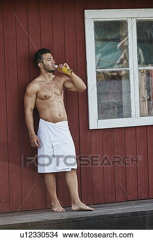 Picture - Young man drinking a beer outside sauna. Fotosearch