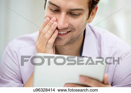 Picture - Young man looking at message on digital tablet. Fotosearch