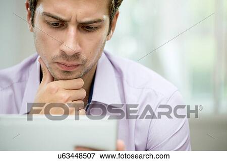 Young man looking at message on digital tablet View Large Photo Image Stock Photo - Young man looking at message on digital tablet. Fotosearch