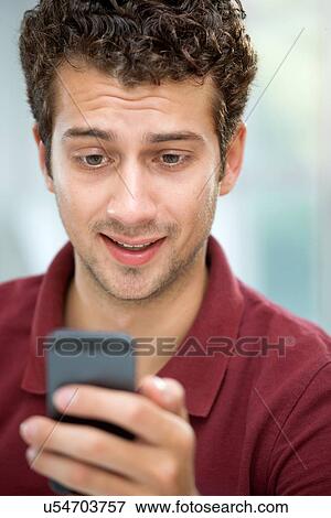 Stock Photo - Young man looking at text message on mobile phone. Fotosearch