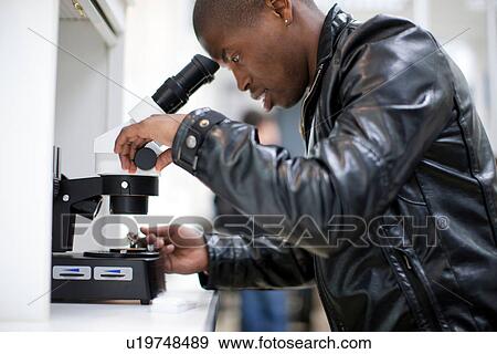 Stock Photo - Young man looking through microscope doing metalwork. Fotosearch
