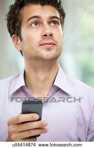 Picture - Young man looking up from mobile phone. Fotosearch