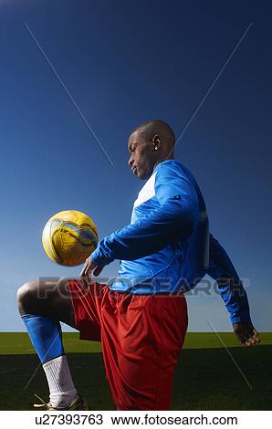 Stock Image - Young man playing keepy uppy with football. Fotosearch