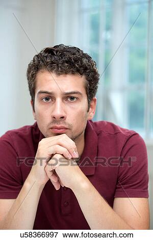 Stock Photo - Young man resting chin on clasped hands. Fotosearch