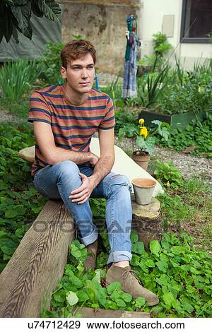 Stock Photo - Young man sitting by vegetable garden. Fotosearch