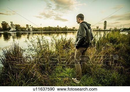 Young man standing on grass looking at water, Russia View Large Photo Image Stock Image - Young man standing on grass looking at water, Russia. Fotosearch