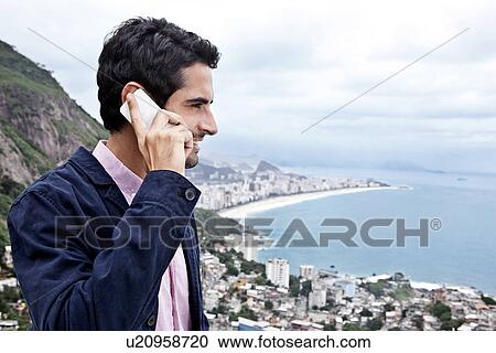 Stock Image - Young man using mobile phone, Casa Alto Vidigal, Rio De Janeiro, Brazil. Fotosearch