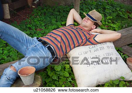 Stock Photograph - Young man wearing straw hat lying on sack. Fotosearch