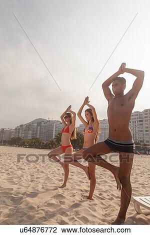 Stock Image - Young people practising yoga on Copacabana Beach, Rio de Janeiro, Brazil. Fotosearch