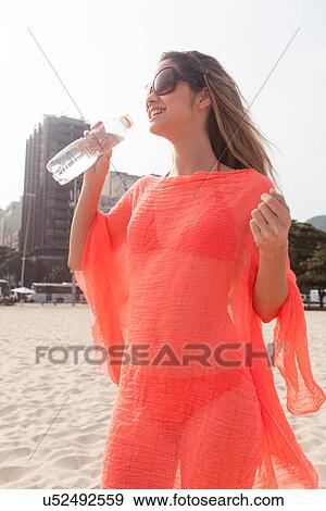 Young woman about to drink from bottle on beach View Large Photo Image Stock Photo - Young woman about to drink from bottle on beach. Fotosearch