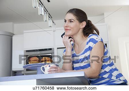 Stock Photo - Young woman at breakfast bar with coffee and cell phone. Fotosearch