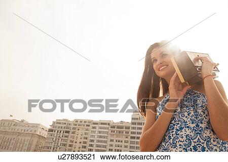 Stock Image - Young woman carrying radio on shoulder, Copacabana Beach, Rio De Janeiro, Brazil. Fotosearch