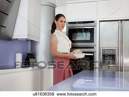 Stock Photo - Young woman holding roasting dish in kitchen. Fotosearch