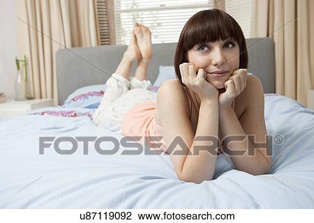 Young woman lying on bed resting on elbows View Large Photo Image Stock Image - Young woman lying on bed resting on elbows. Fotosearch