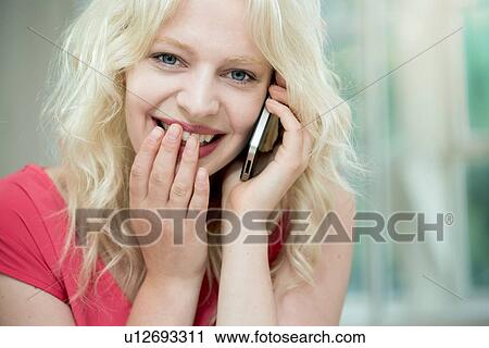 Stock Image - Young woman on cellphone, giggling. Fotosearch