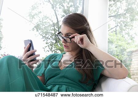 Young woman peering over glasses with cell phone View Large Photo Image Stock Photo - Young woman peering over glasses with cell phone. Fotosearch