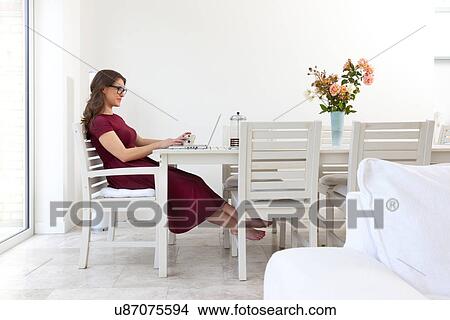 Young woman sitting at table using laptop View Large Photo Image Picture - Young woman sitting at table using laptop. Fotosearch