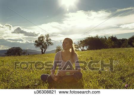 Young woman sitting cross legged in field daydreaming View Large Photo Image Stock Image - Young woman sitting cross legged in field daydreaming. Fotosearch