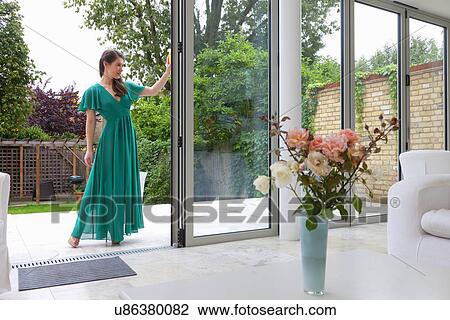 Stock Image - Young woman standing in patio dorrway. Fotosearch