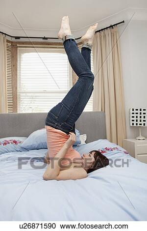 Stock Image - Young woman struggling to zip jeans on bed. Fotosearch