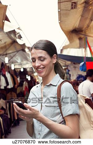 Stock Image - Young woman texting on cell phone, San Lorenzo market, Florence, Tuscany, Italy. Fotosearch