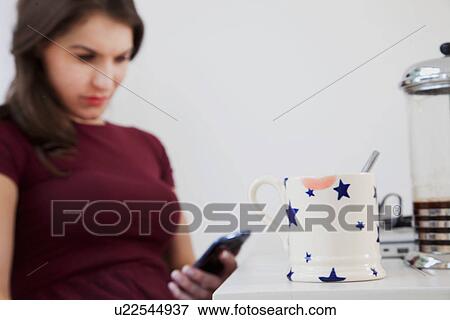 Young woman using cell phone with coffee mug in foreground View Large Photo Image Stock Photo - Young woman using cell phone with coffee mug in foreground. Fotosearch