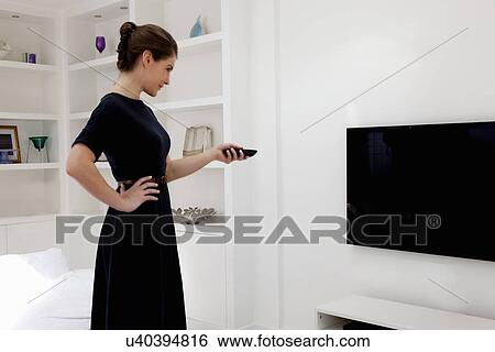 Stock Photograph - Young woman wearing black dress switching on tv. Fotosearch
