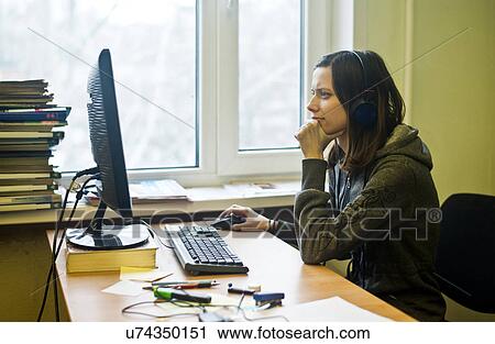 Stock Image - Young woman wearing headphones using computer. Fotosearch