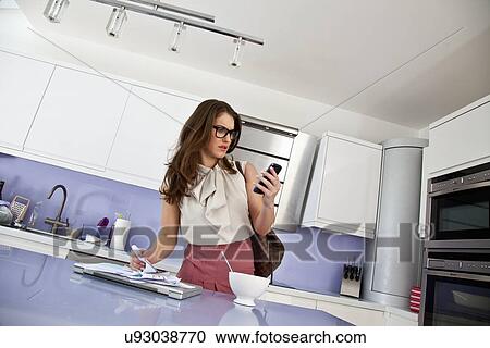 Stock Image - Young woman with cell phone and paperwork at breakfast. Fotosearch