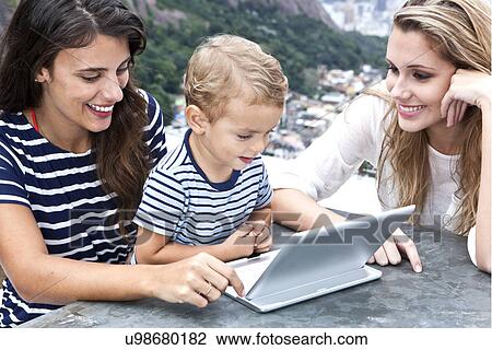 Stock Image - Young women and toddler looking at laptop, Casa Alto Vidigal, Rio De Janeiro, Brazil. Fotosearch