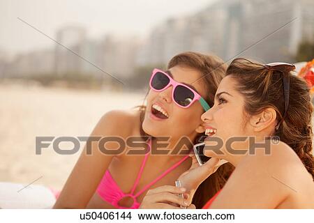 Picture - Young women chatting on mobile phone on beach. Fotosearch