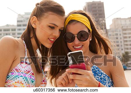 Stock Photograph - Young women smiling at text on mobile phone. Fotosearch