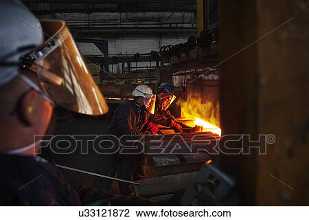 Stock Image - 100mm square steel billet is removed from furnace as cold steel billet waits to be heated, with furnace door operator in foreground. Fotosearch