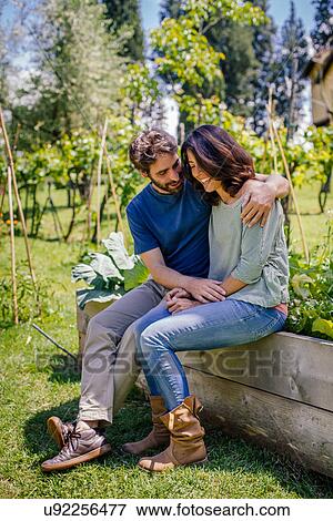 Affectionate mid adult couple sitting in garden View Large Photo Image Stock Photo - Affectionate mid adult couple sitting in garden. Fotosearch